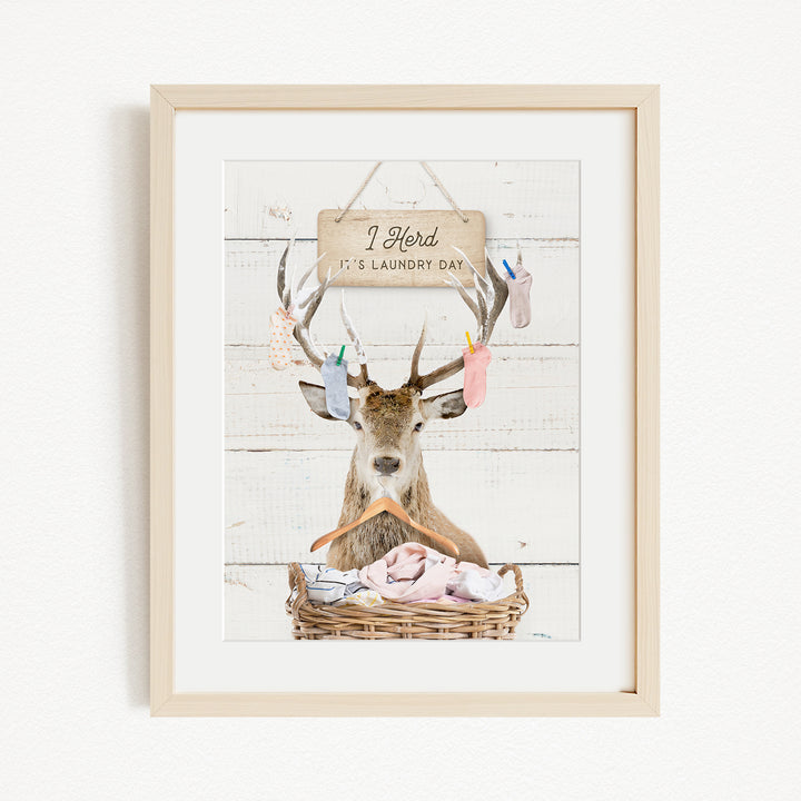 A framed image depicting a deer with antlers hanging from its head, holding a basket filled with clothes, and a sign above it that says "I hold it's laundry day".