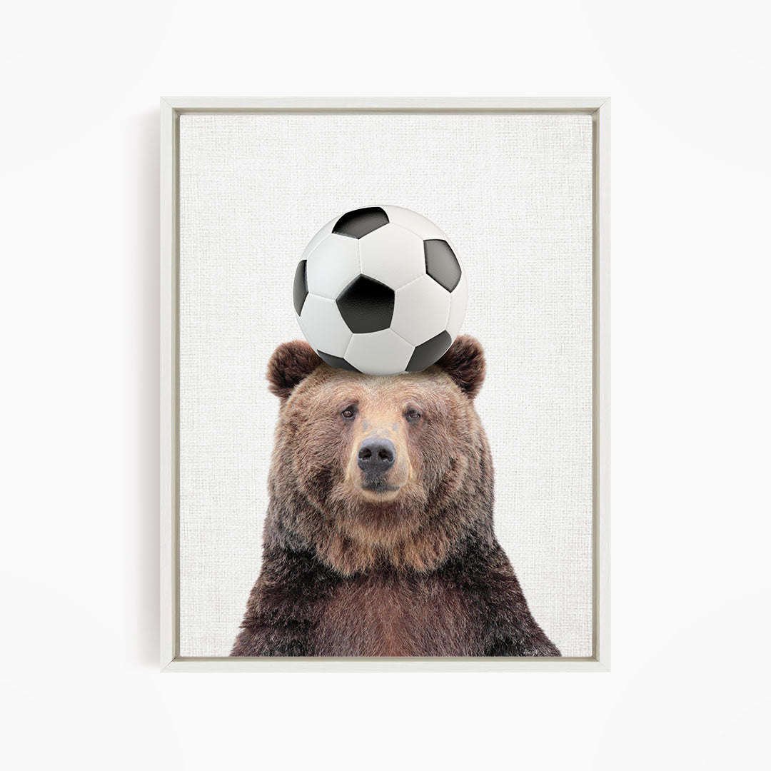 A brown bear balancing a soccer ball on its head.