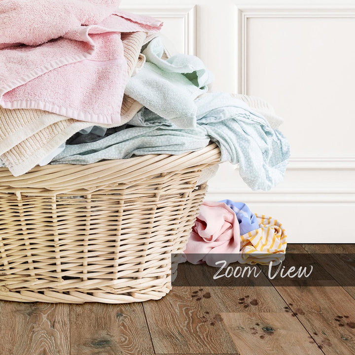 A wicker basket filled with various folded clothes sits on a wooden floor, with a white door visible in the background.