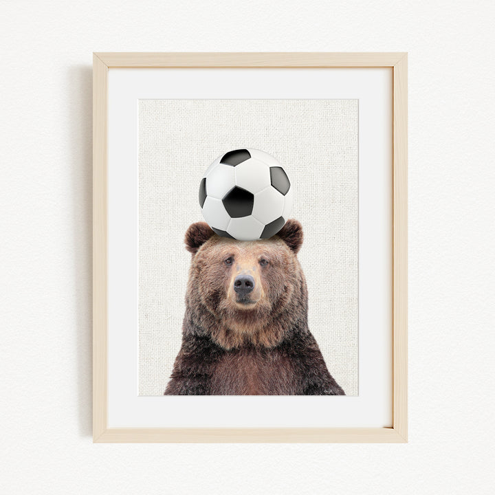 A brown bear balancing a soccer ball on its head.
