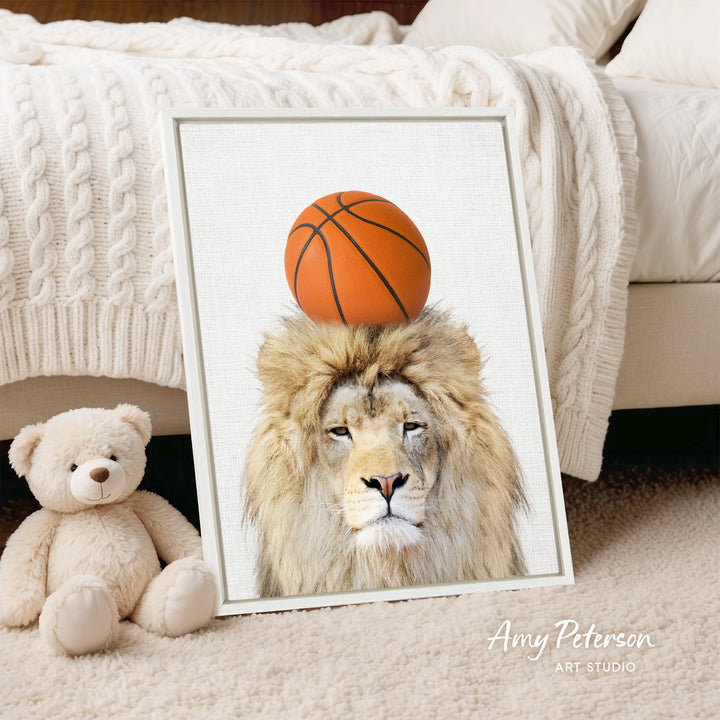 A framed image of a lion with a basketball on its head, placed on a bed next to a stuffed teddy bear.