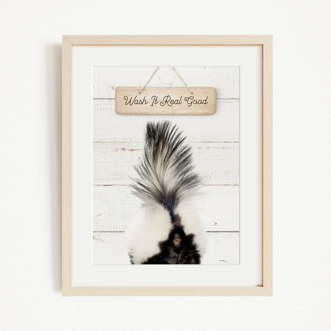 A framed image of a skunk's tail against a white wooden background, with a wooden sign above it that says "Wash It Real Good".