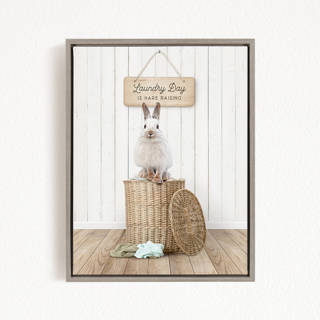 A white rabbit sits atop a wicker basket, with a wooden sign above that reads "Laundry Day is Hard Raising".