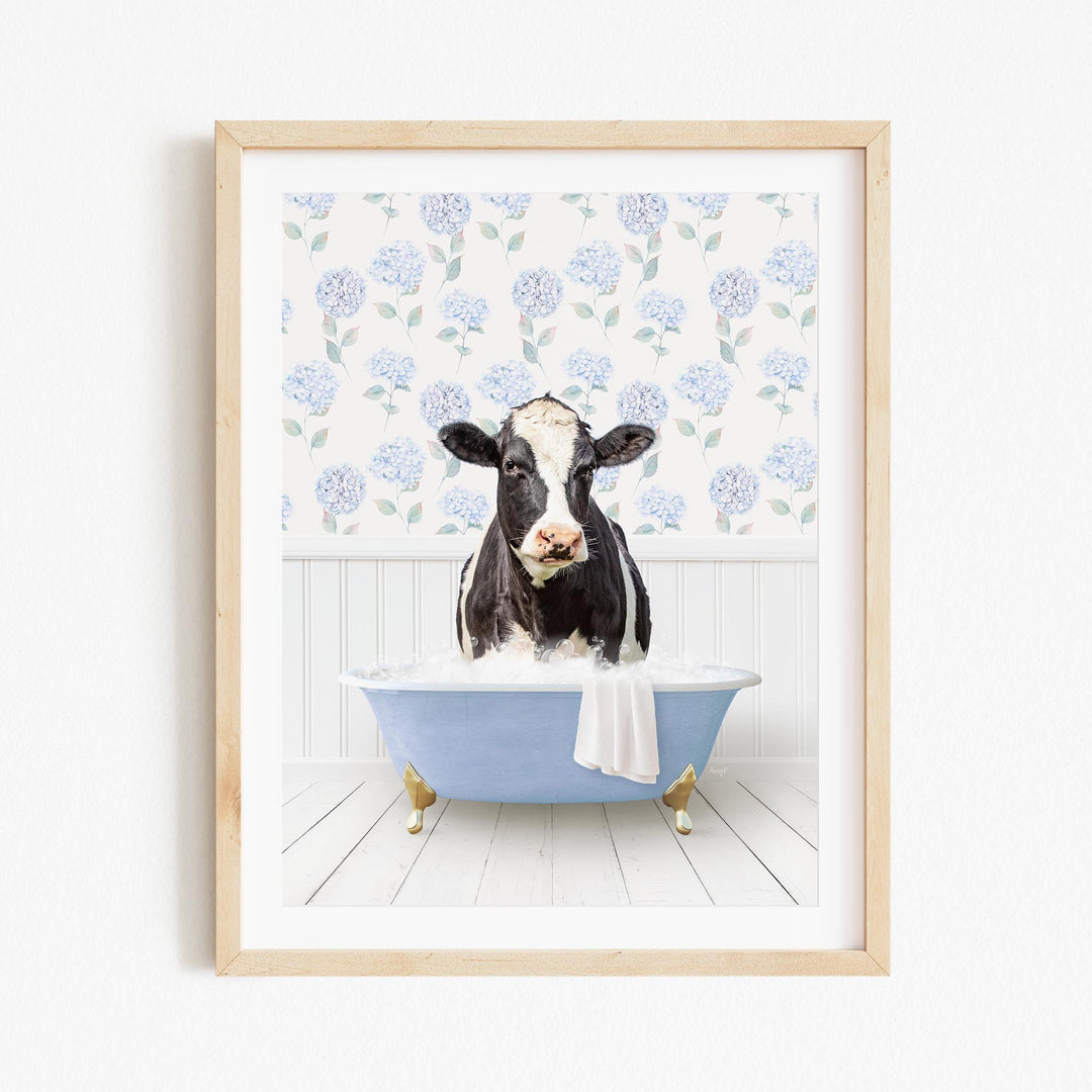 A black and white cow is sitting in a blue bathtub filled with bubbles, surrounded by a floral pattern on the wall behind it.