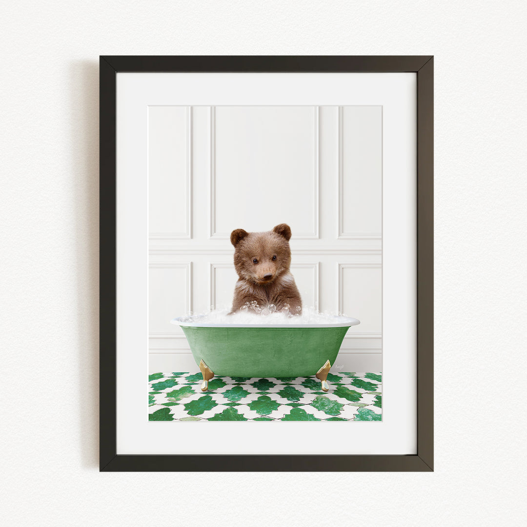 A small brown bear is sitting in a green bathtub filled with water, surrounded by a green and white patterned rug.