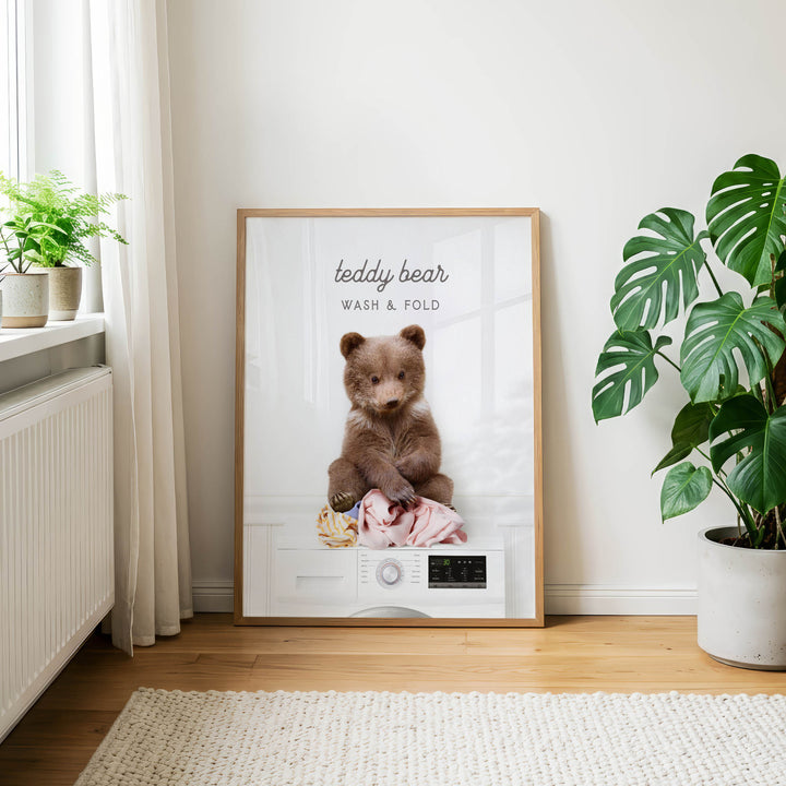 A framed poster featuring a teddy bear sitting on a washing machine, with the text "teddy bear WASH & FOLD" displayed on the poster.