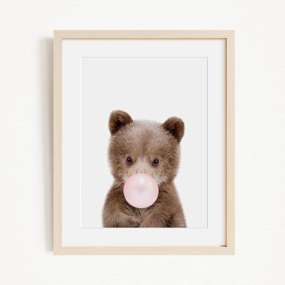 A cute brown bear is blowing a bubble with a pink bubble gum bubble.