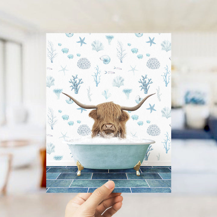 A hand is holding up a print featuring a large, horned animal, likely a yak, sitting in a bathtub filled with bubbles, surrounded by a pattern of seashells and starfish.