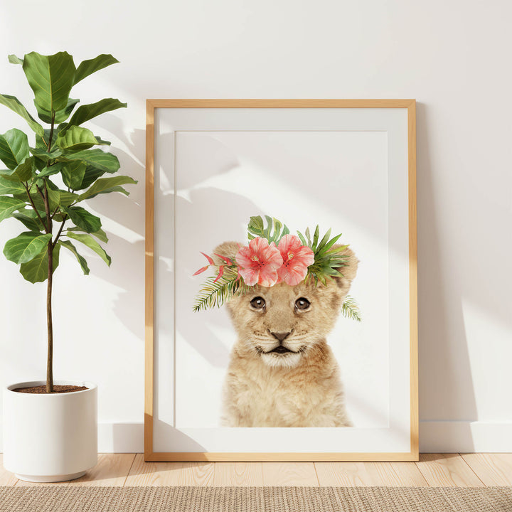 A framed print of a young lion cub with a floral headpiece is displayed on a white wall, accompanied by a potted plant to the left.