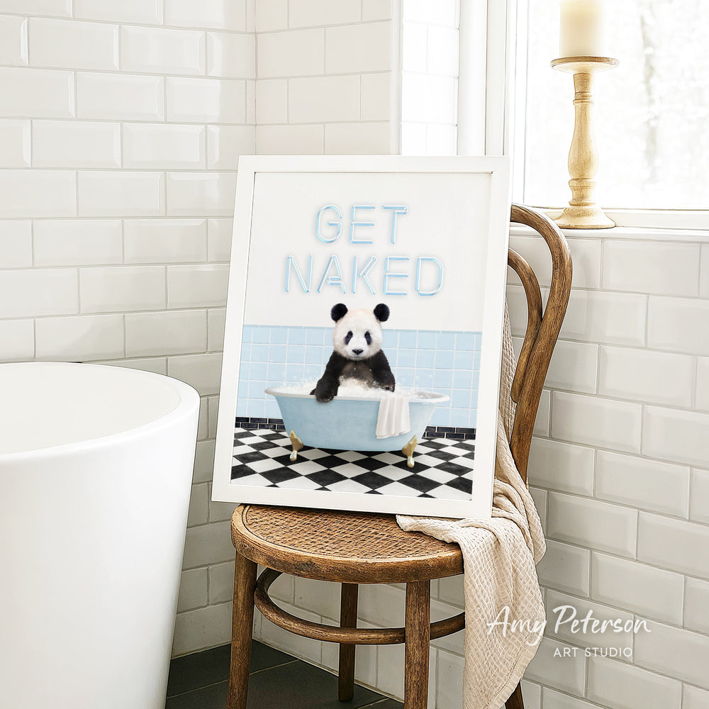 A framed print featuring a panda sitting in a bathtub with the text "GET NAKED" on it, placed on a wooden chair in a bathroom setting.