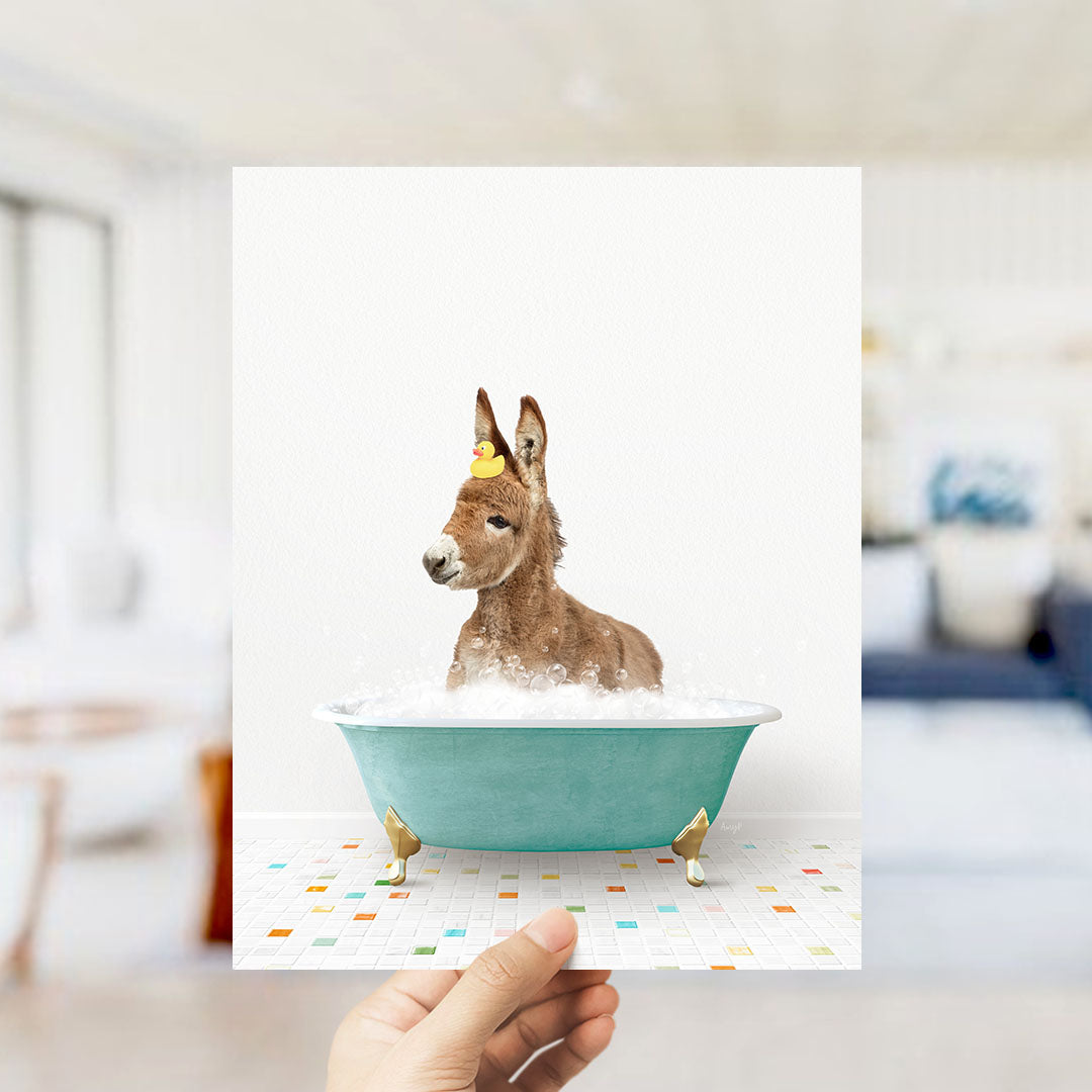 A donkey is sitting in a blue bathtub filled with bubbles, with a yellow rubber duck floating on its head.