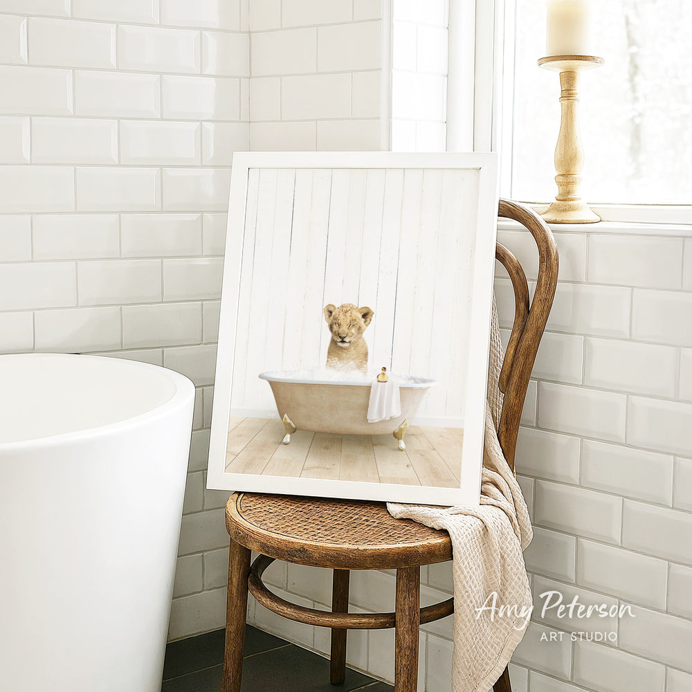 A framed image of a lion sitting in a bathtub, with a towel draped over the back of the chair.