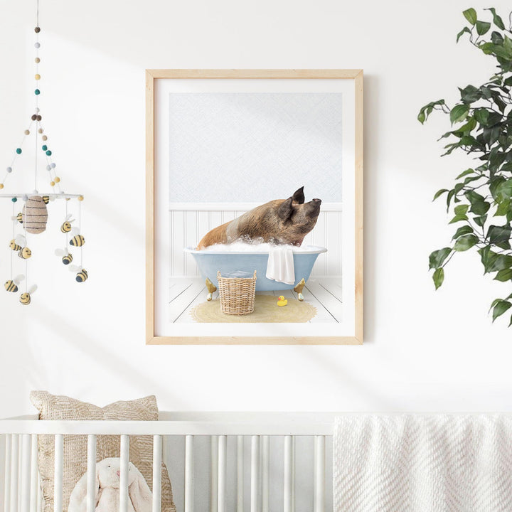 A framed image of a pig sitting in a bathtub, surrounded by a white and blue color scheme, is displayed on a white wall in a nursery setting.