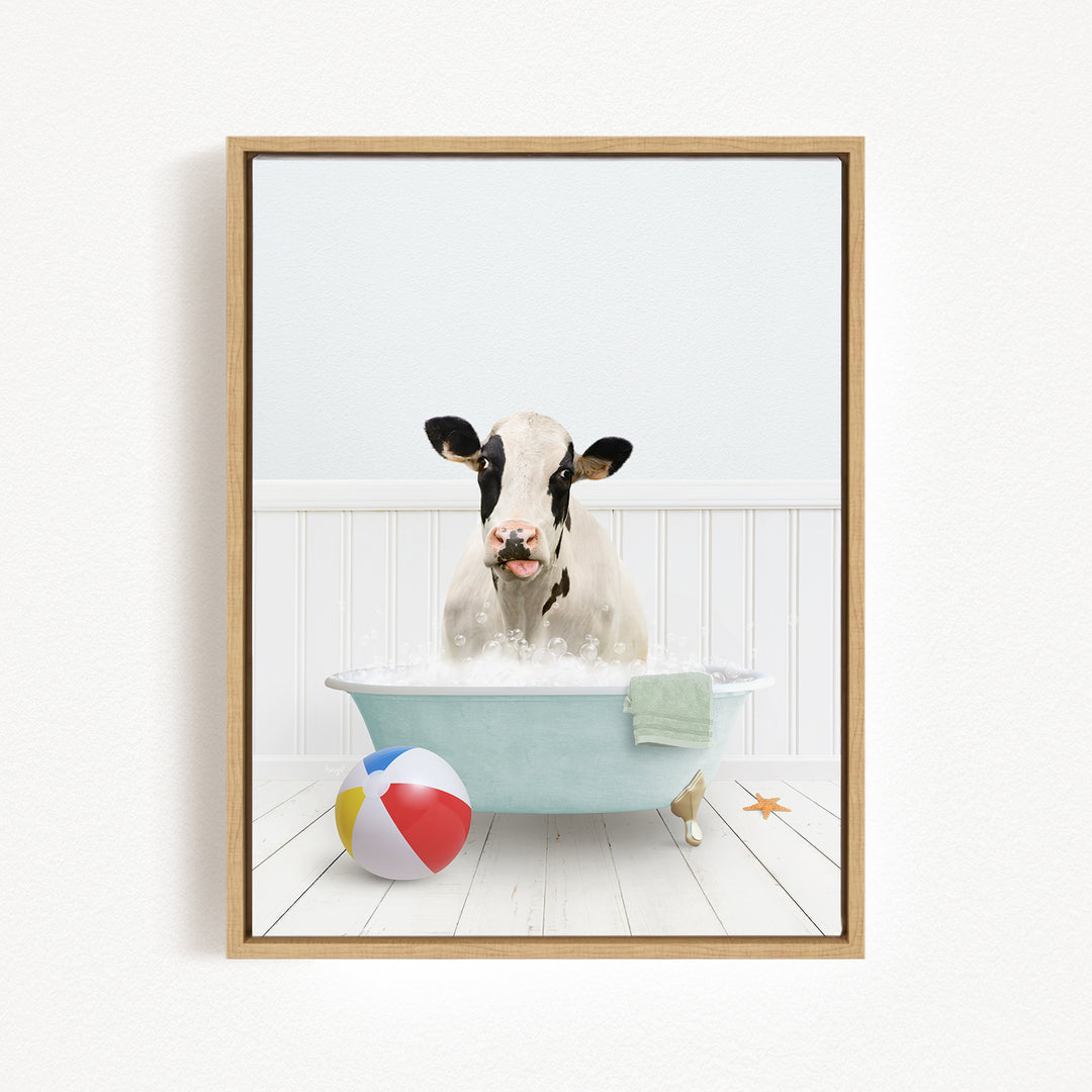 A black and white cow is sitting in a bathtub filled with water, surrounded by a beach ball and a towel.
