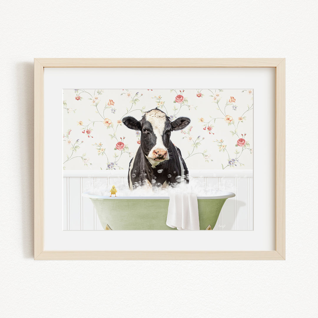 A black and white cow is sitting in a green bathtub filled with bubbles, with a floral wallpaper in the background.