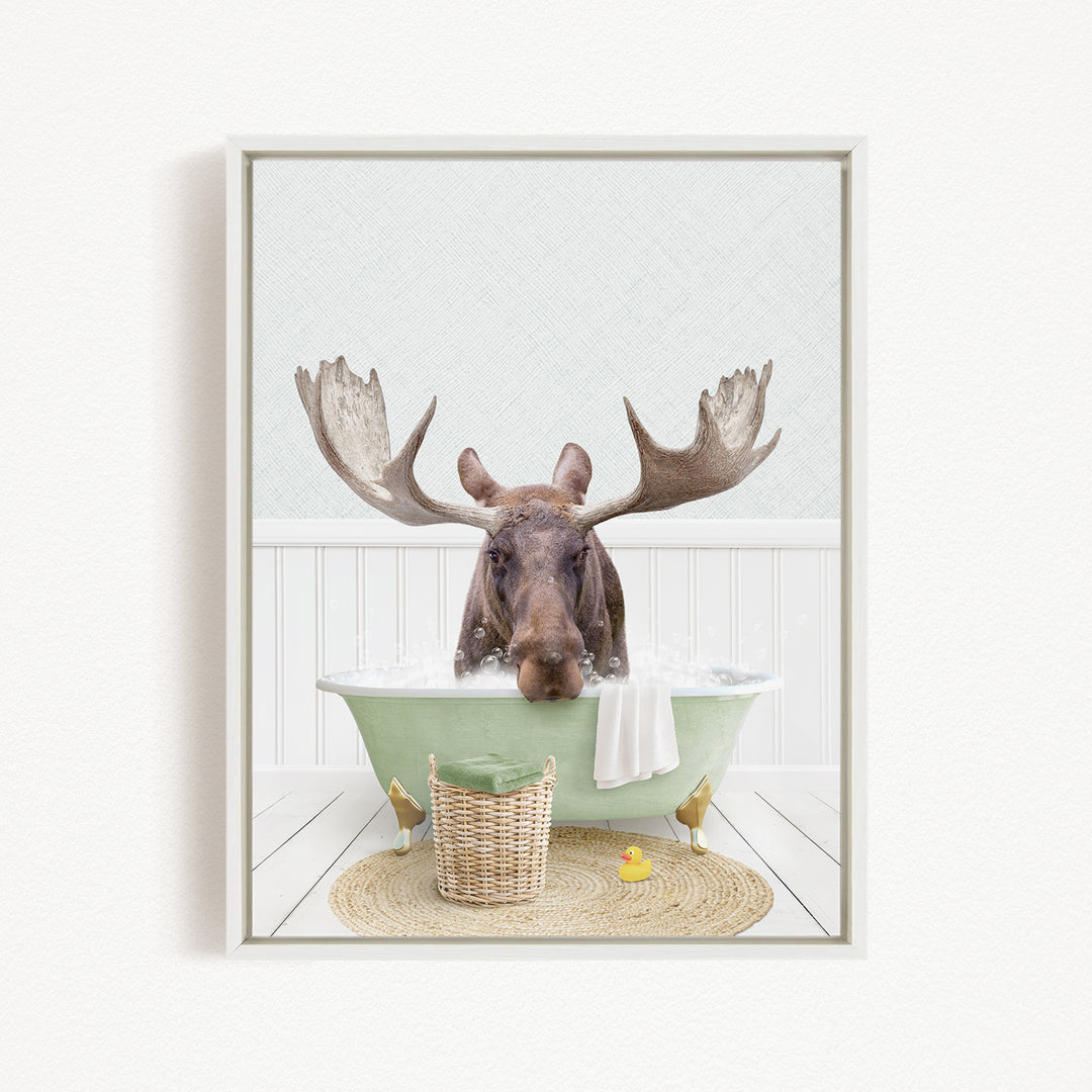 A moose with large antlers is sitting in a green bathtub filled with bubbles, surrounded by a basket of toys and a yellow rubber duck.