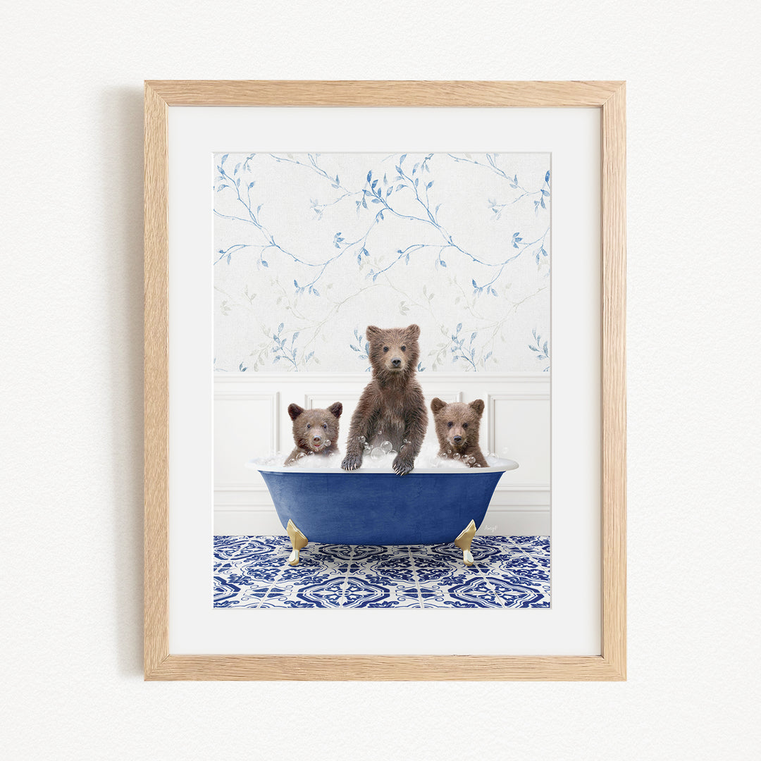 A framed image depicting three brown bears sitting in a blue bathtub, with a patterned tile floor and a floral wallpaper in the background.