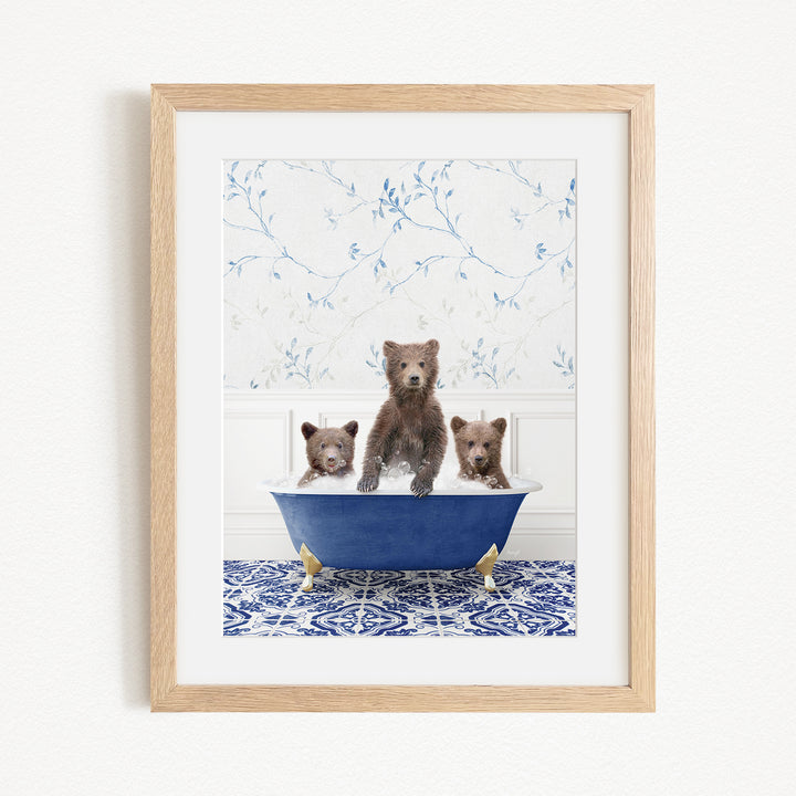 A framed image depicting three brown bears sitting in a blue bathtub, with a patterned tile floor and a floral wallpaper in the background.
