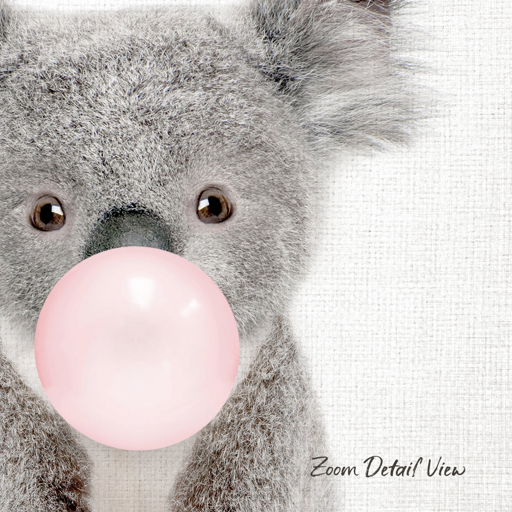 A close-up of a koala bear blowing a pink bubble with its mouth, against a white background.
