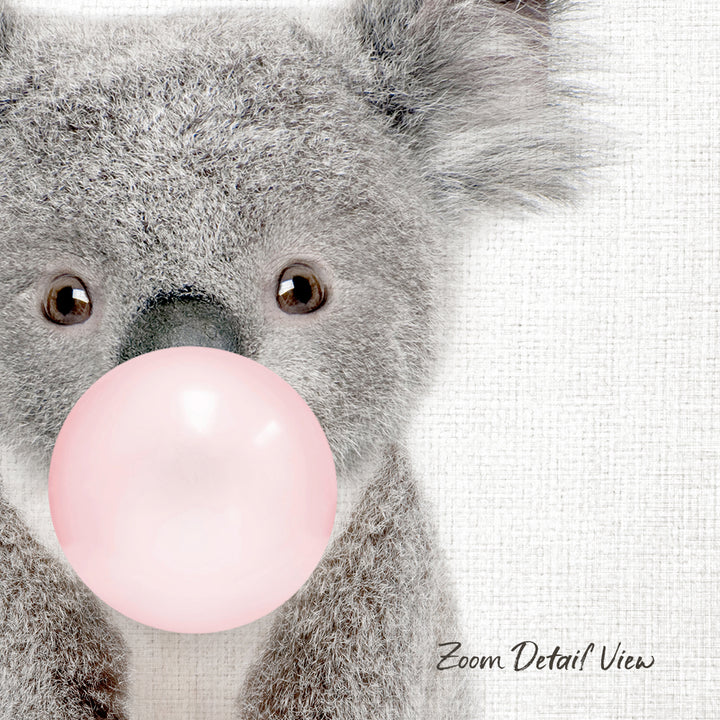 A close-up of a koala bear blowing a pink bubble with its mouth, against a white background.