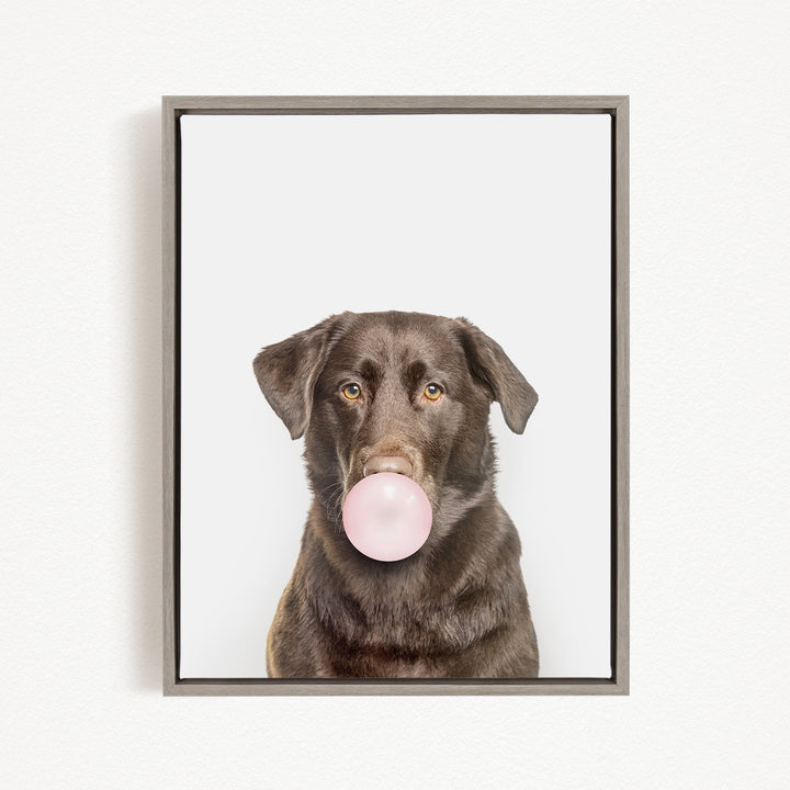 A brown dog is blowing a bubble with a pink bubble gum bubble.
