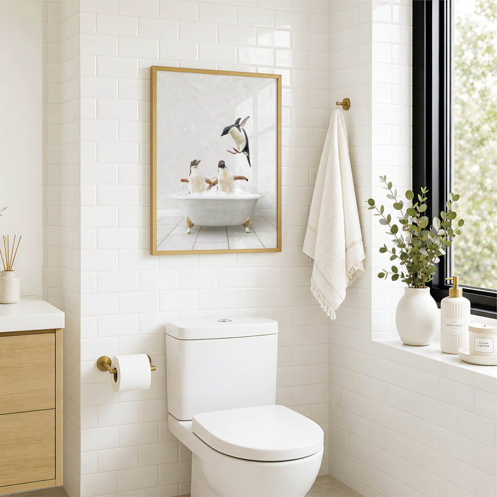 A bathroom with a white toilet, a framed picture of penguins in a bathtub, and a window with greenery on the sill.