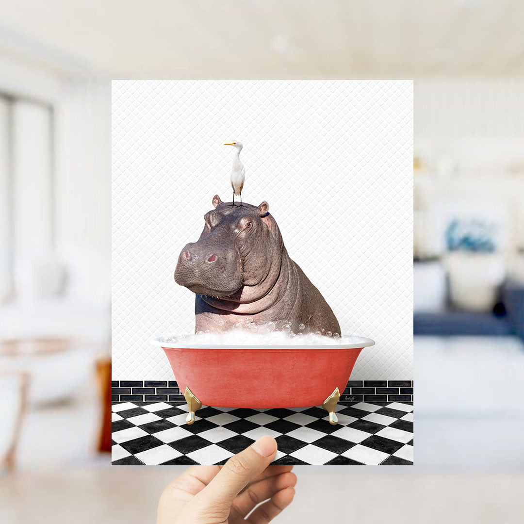 A hand holds up a framed image depicting a hippopotamus sitting in a red bathtub, with a seagull perched on its head.