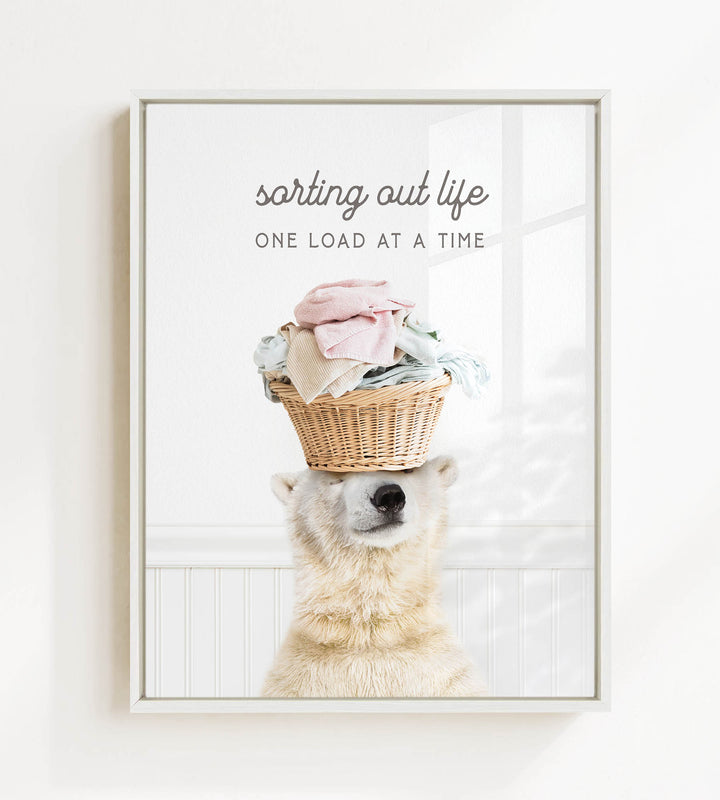 A polar bear balancing a basket of laundry on its head, with the text "sorting out life" and "ONE LOAD AT A TIME" displayed above the image.