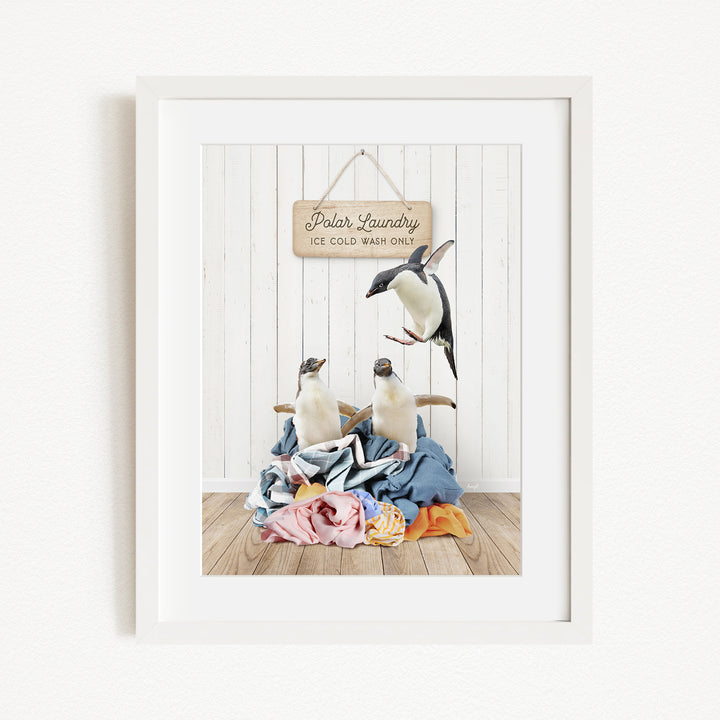 A framed image of two penguins sitting on a pile of clothes, with a sign above them that reads "Polar Laundry".