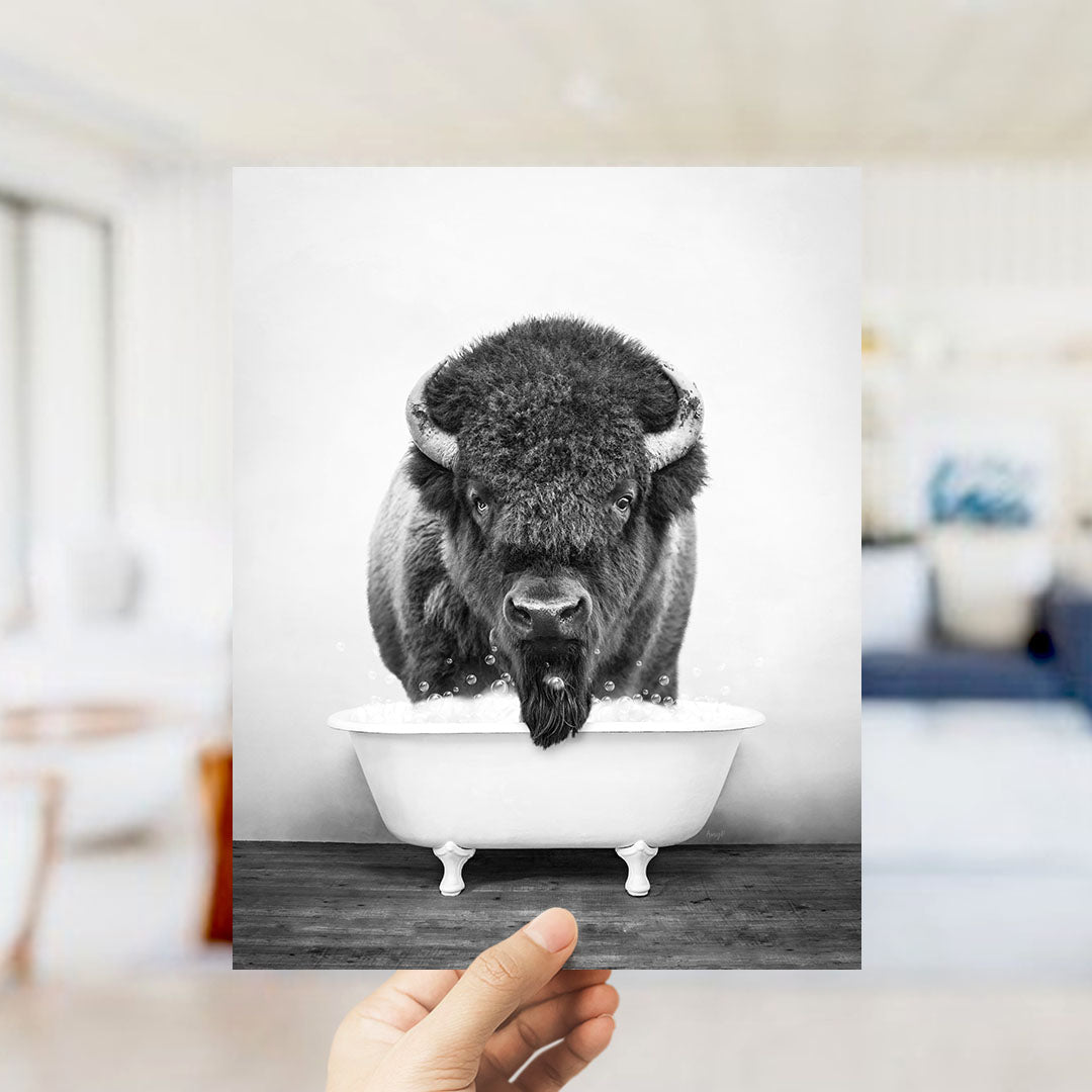 A black and white photograph of a bison standing in a bathtub, with a blurred background suggesting an indoor setting.