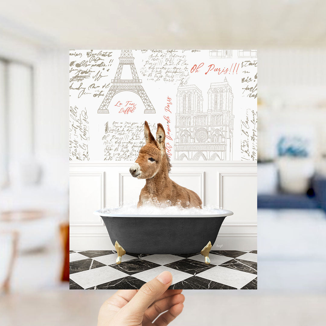 A hand holds up a collage of images featuring a donkey sitting in a bathtub, with the Eiffel Tower and Parisian architecture visible in the background.