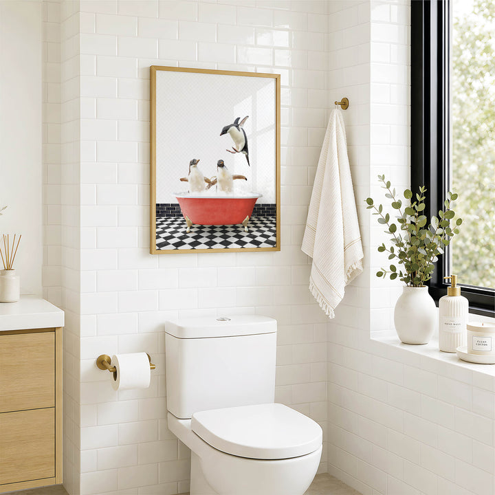 A bathroom with a white toilet, a framed picture of penguins in a bathtub, and a window with greenery on the sill.