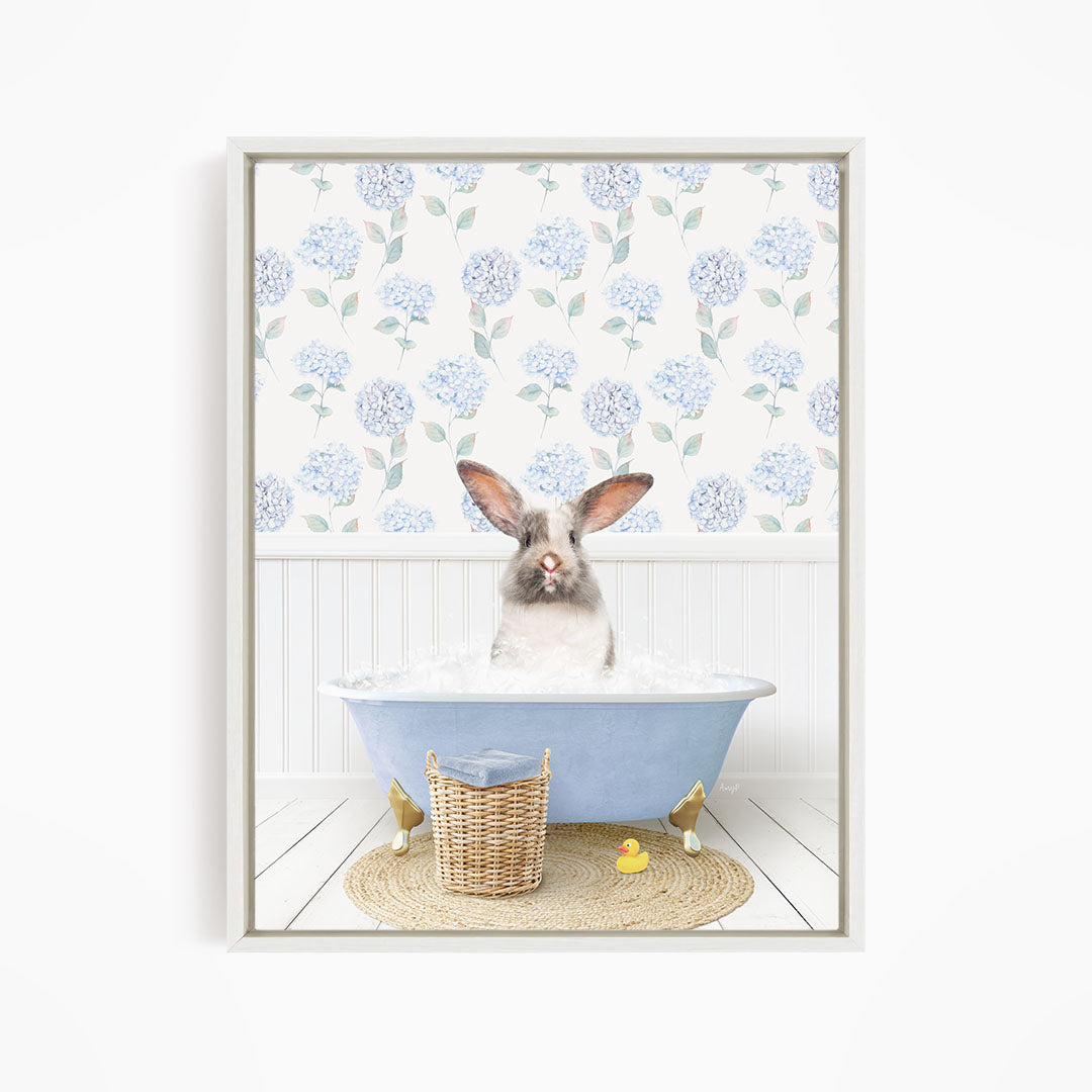 A rabbit sitting in a blue bathtub filled with water, surrounded by a wicker basket and a yellow rubber duck.