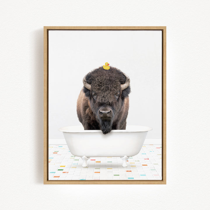 A buffalo with a yellow rubber duck perched on its head is standing in a white bathtub, with a colorful tiled floor in the background.