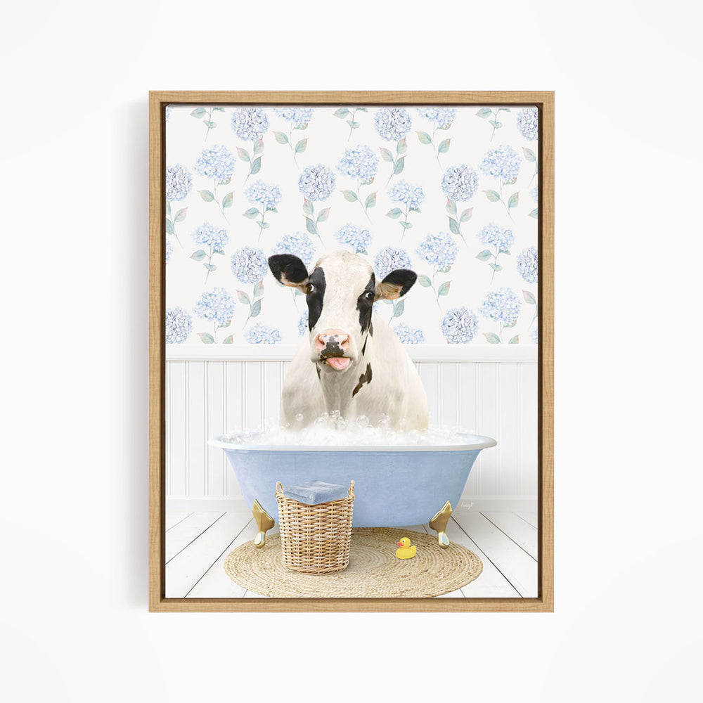 A black and white cow is sitting in a blue bathtub filled with bubbles, surrounded by a wicker basket and rubber ducks.