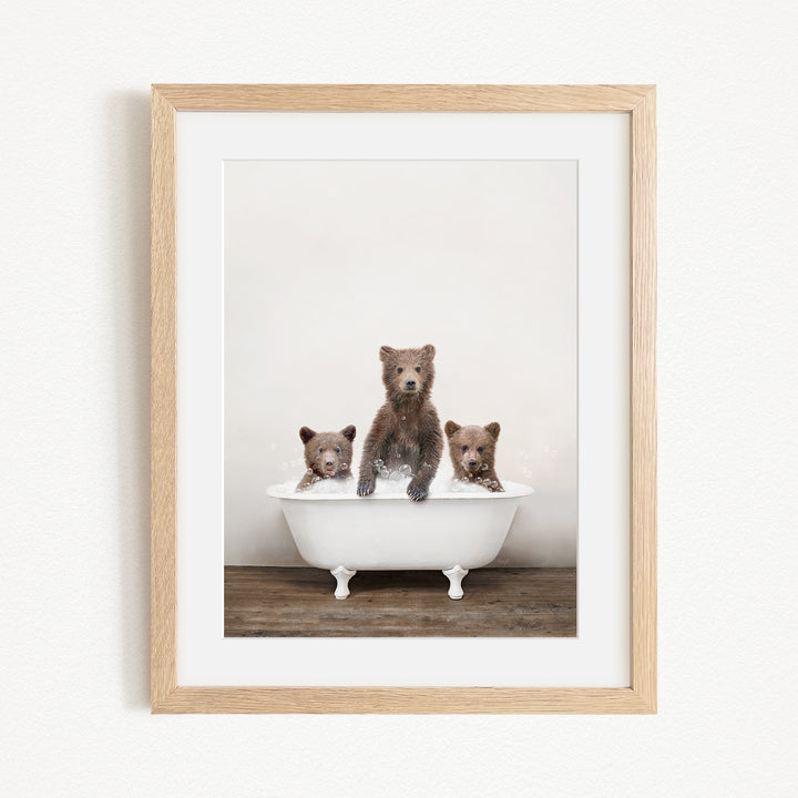 A framed image depicting three brown bears sitting in a white bathtub, with one bear sitting in the center and the other two bears sitting on either side.
