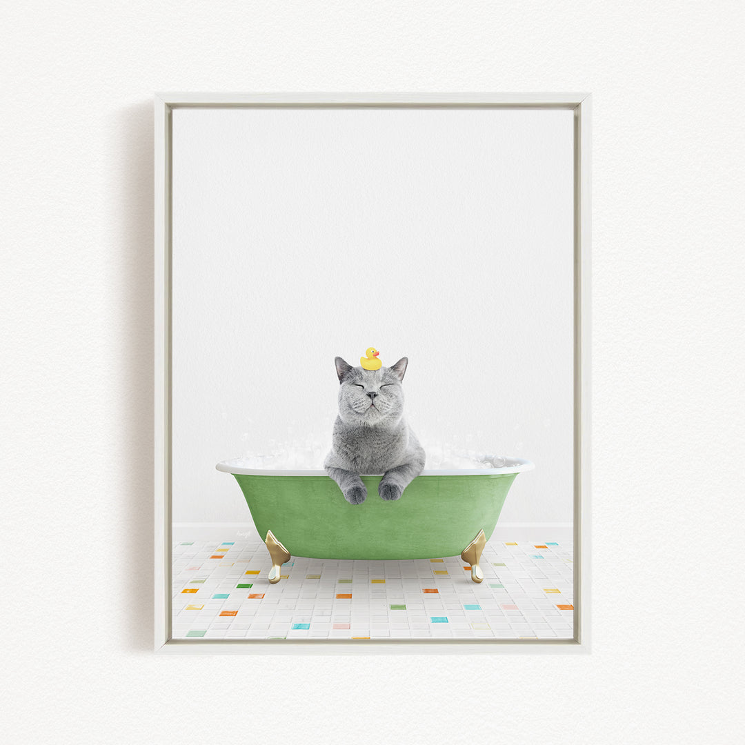 A gray cat sitting in a green bathtub filled with bubbles, wearing a yellow rubber duck hat.
