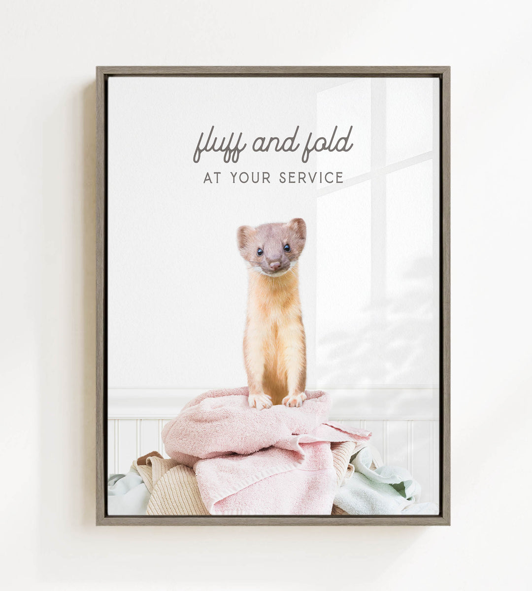 A small brown and white ferret sitting on a pile of clothes, with the text "fluff and fold at your service" written above the image.