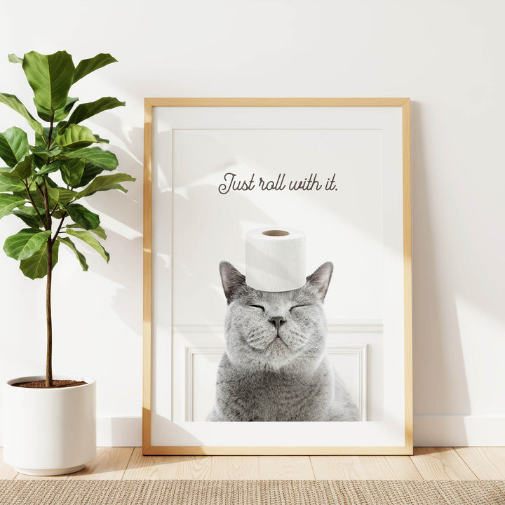 A framed image of a cat with its eyes closed, wearing a roll of toilet paper on its head, and the text "Just roll with it."