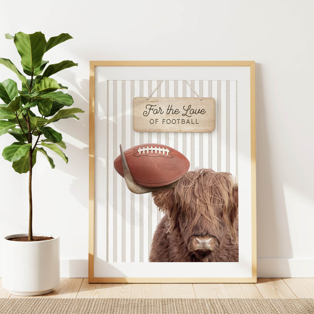 a framed poster with a picture of a Highland cow holding a football, accompanied by a wooden sign that reads "For the Love of Football".