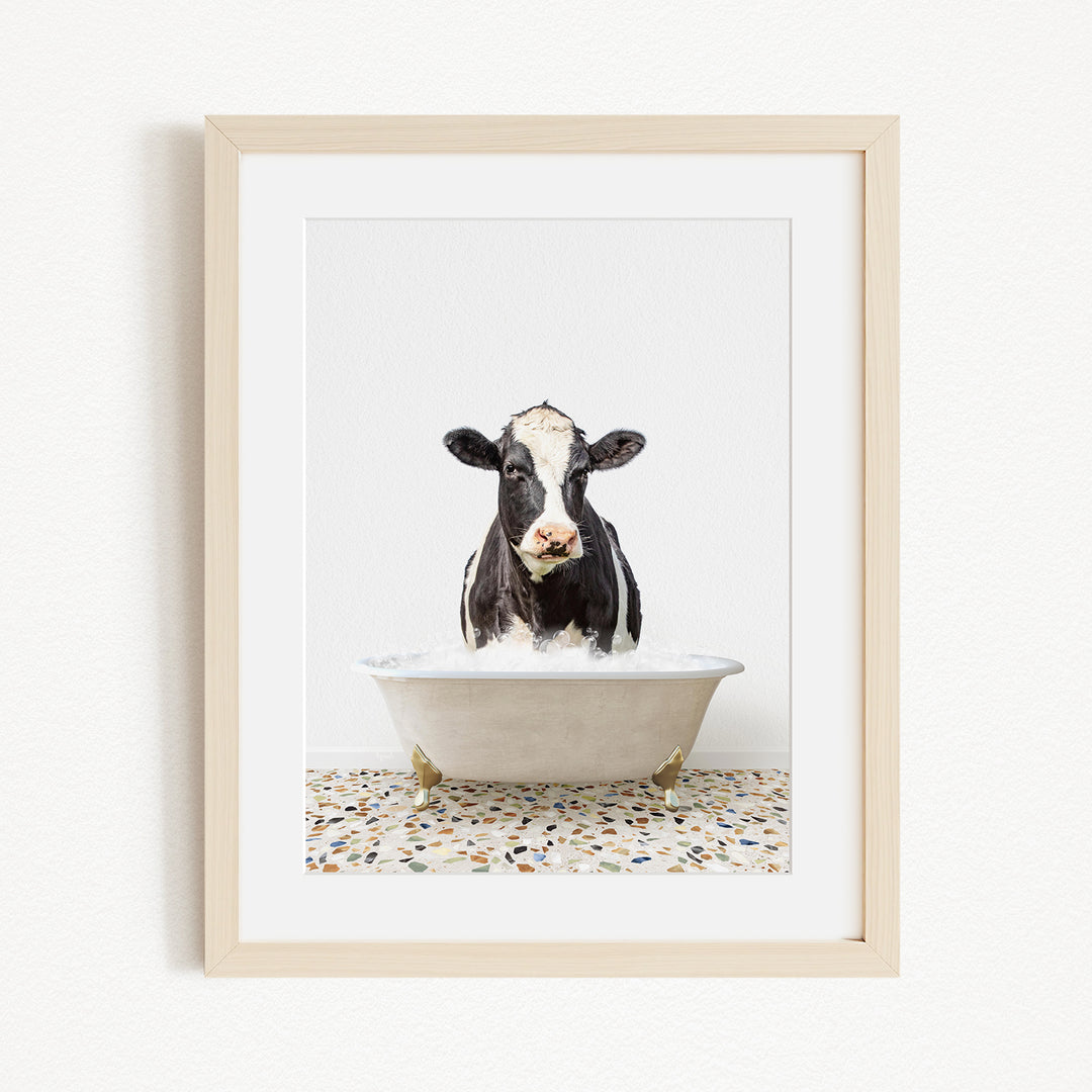 A black and white cow is sitting in a white bathtub filled with water, creating a whimsical and humorous scene.