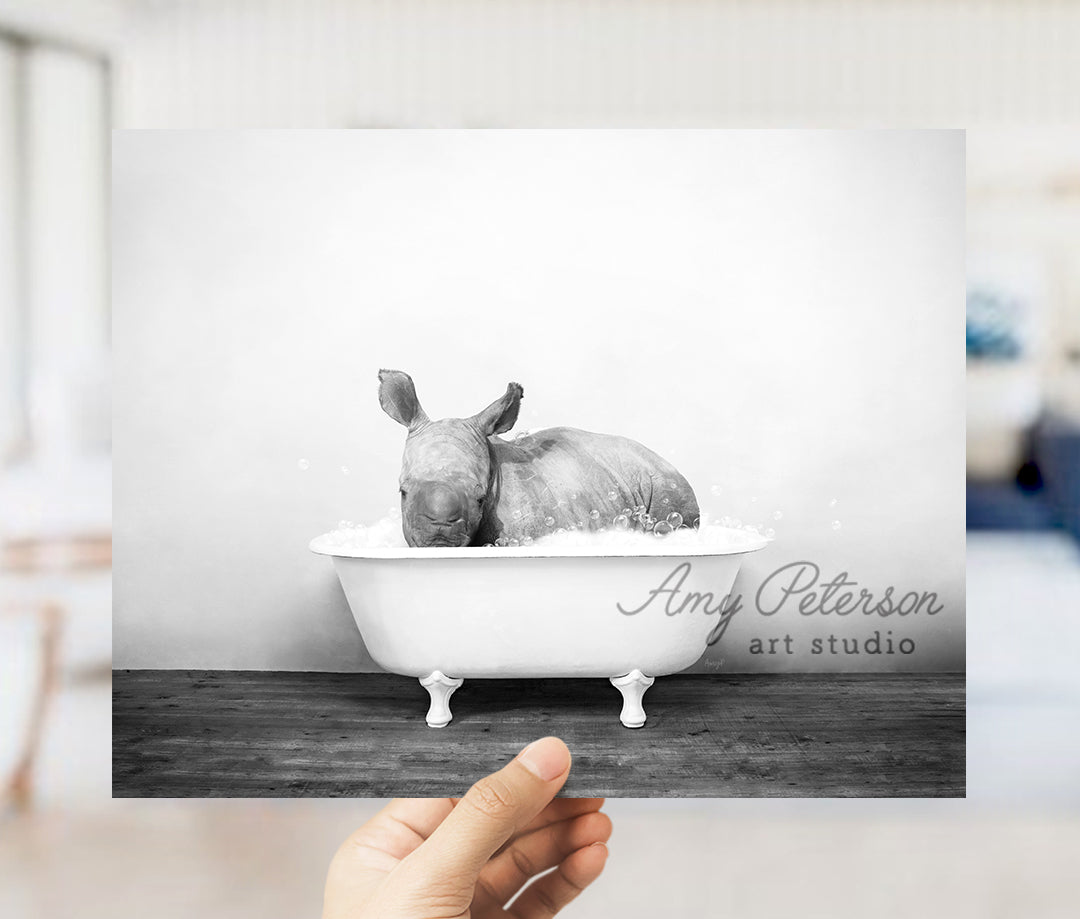 a hand holding up a black and white photo of a rhino in a bathtub