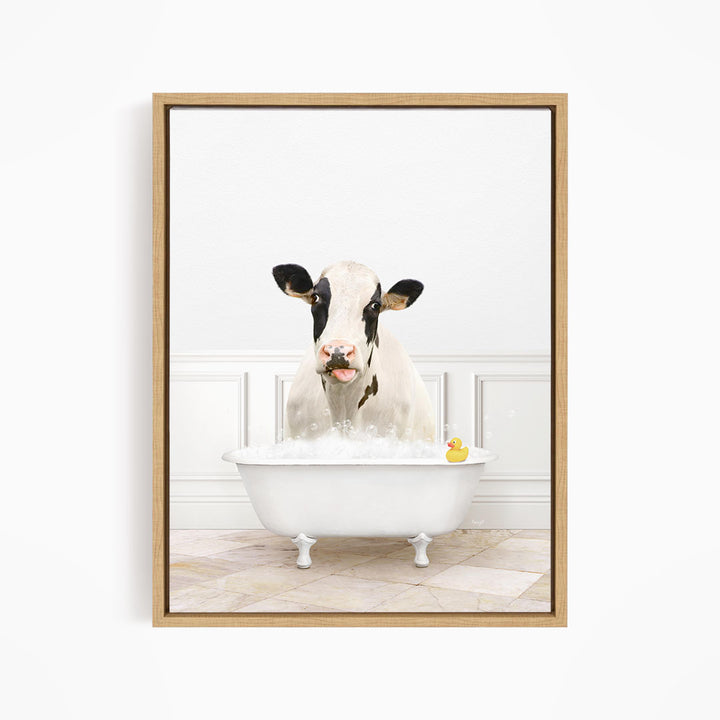 A black and white cow is sitting in a white bathtub filled with bubbles, with a rubber duck floating in the water.
