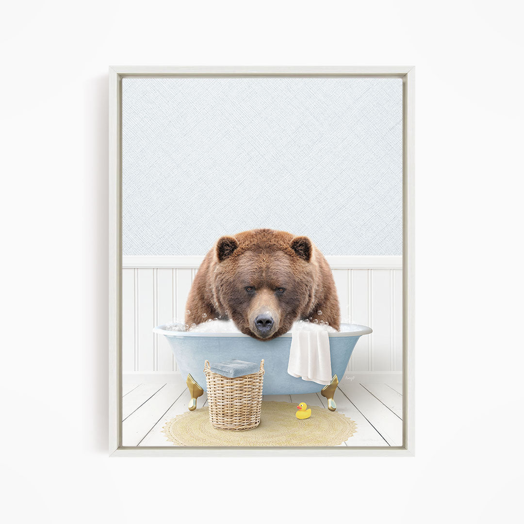 A brown bear is sitting in a blue bathtub filled with water, surrounded by a yellow rubber duck and a white towel.