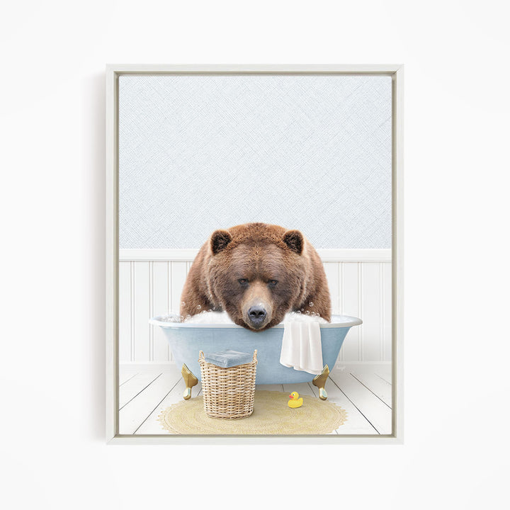 A brown bear is sitting in a blue bathtub filled with water, surrounded by a yellow rubber duck and a white towel.