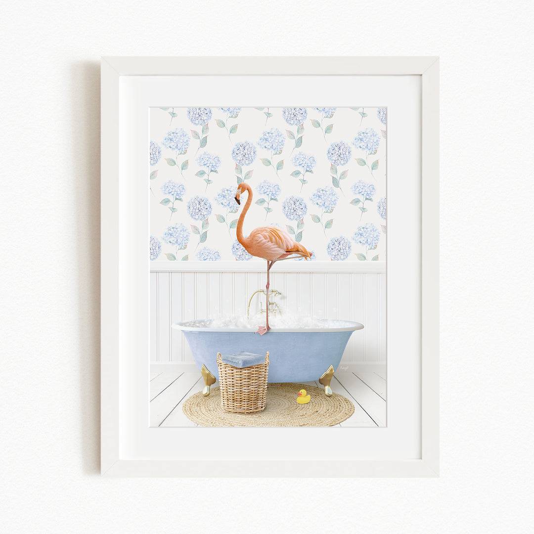 A framed image depicting a pink flamingo standing on a blue bathtub in a bathroom with a blue and white floral pattern on the wall behind it.
