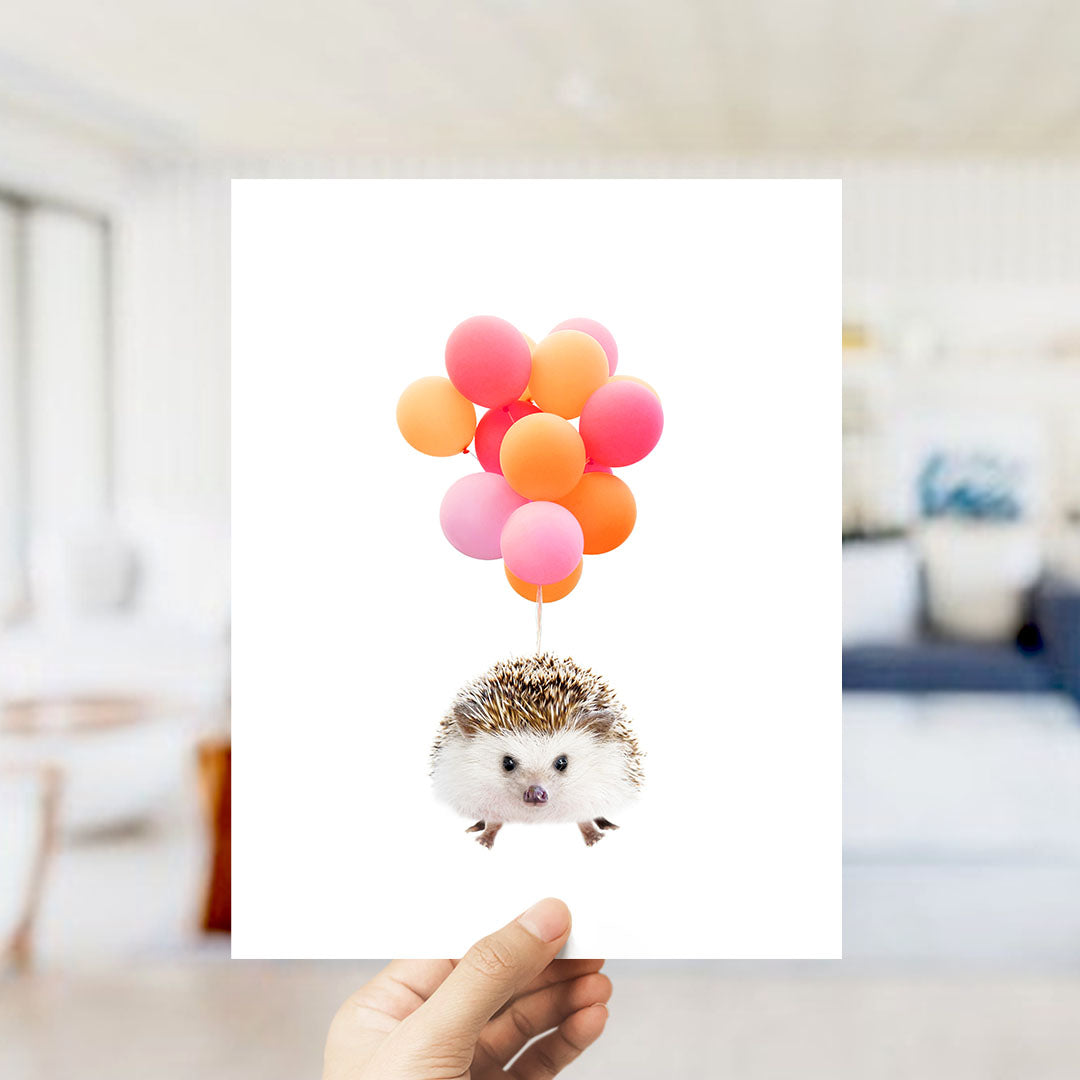 A person is holding a piece of paper with a hedgehog image on it, surrounded by colorful balloons.