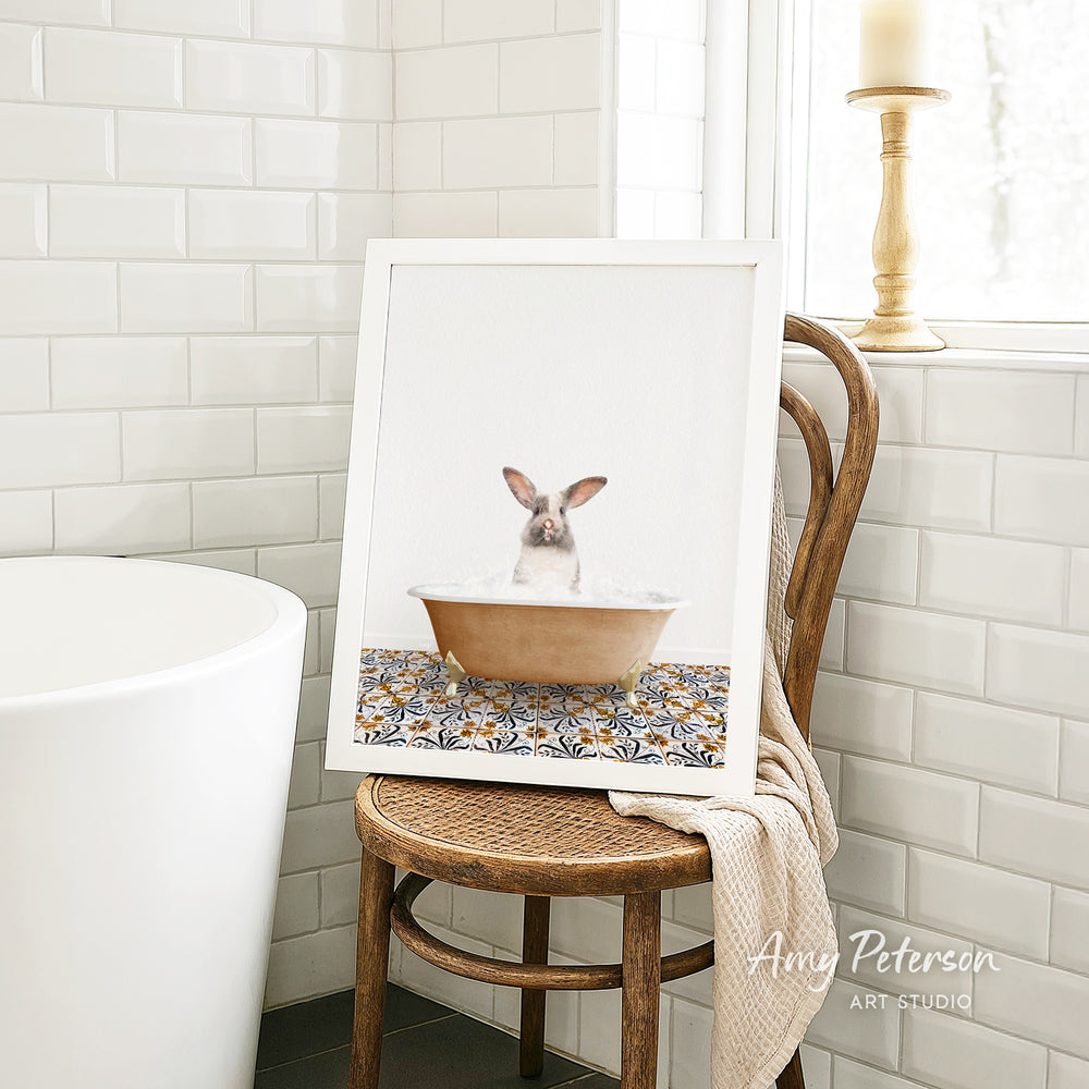 A framed image of a rabbit sitting in a bathtub, surrounded by a patterned design, is displayed on a wooden chair in a bathroom setting.