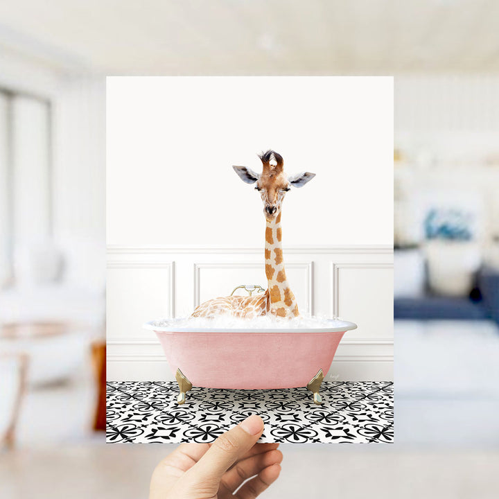 A giraffe sitting in a pink bathtub filled with bubbles, with a hand holding the image up to the camera.