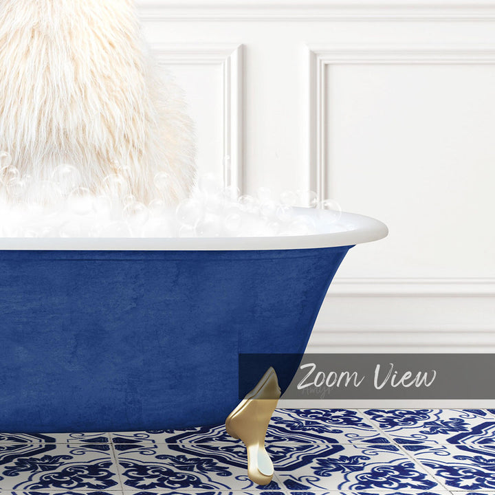 A fluffy white dog is sitting in a blue bathtub filled with bubbles, with a gold claw-like object on the floor.